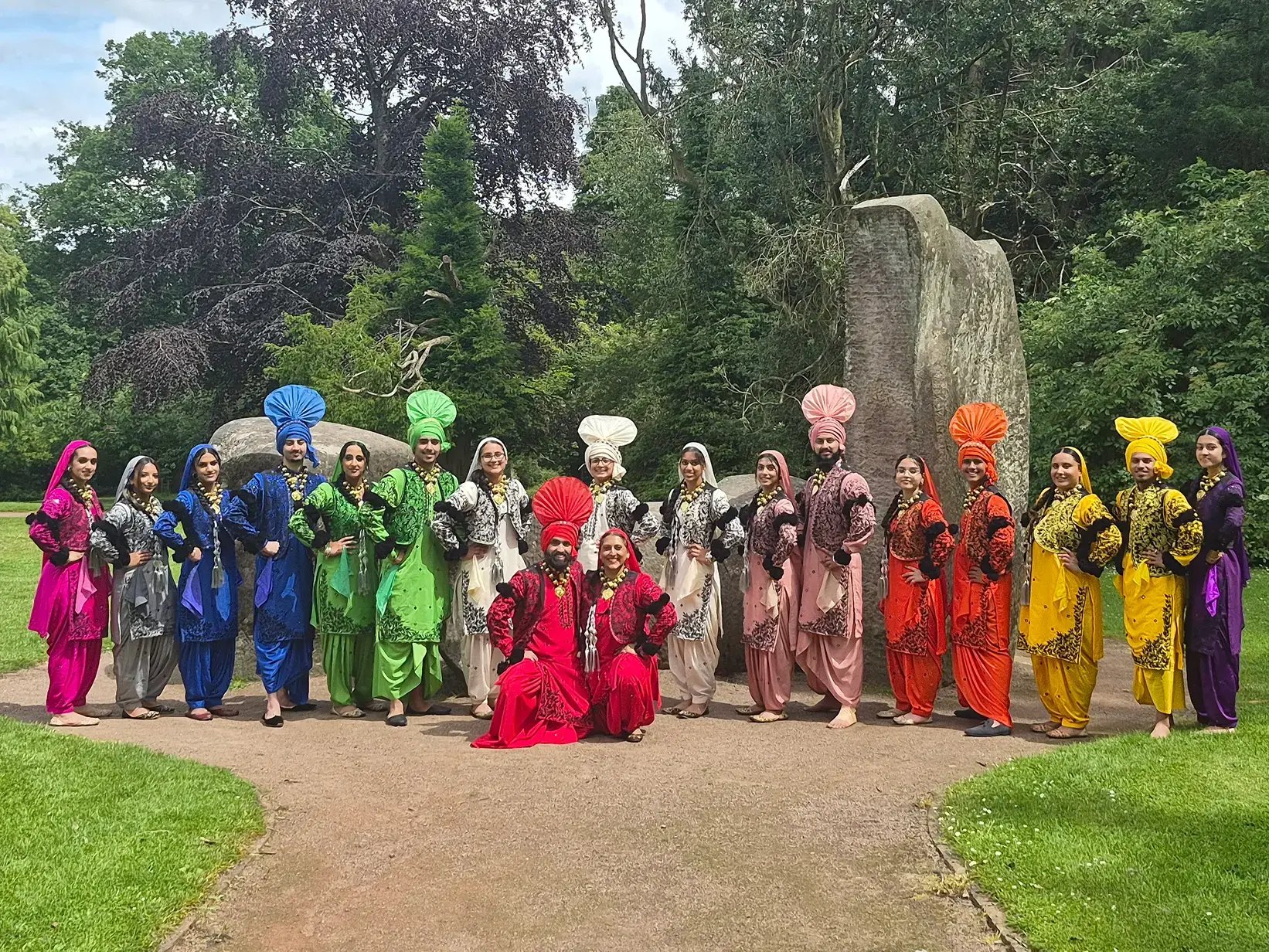 Large Bhangra dance group posing outdoors in colourful traditional Punjabi costumes and turbans.