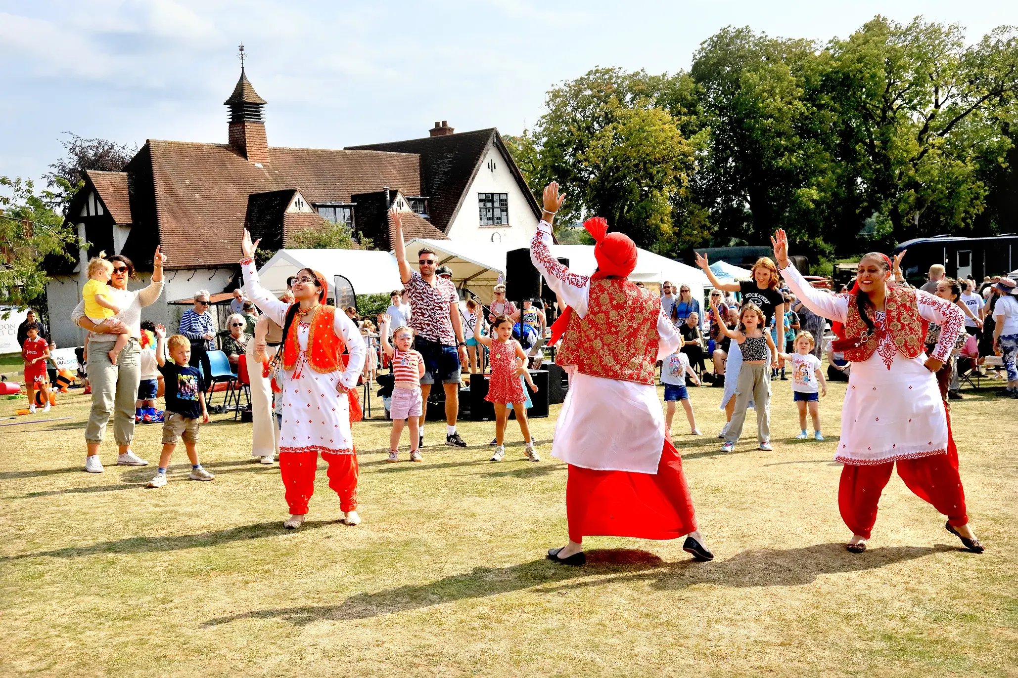 Jodi Dancers in costume leading families and children in bhangra on the field at Sandon Fete