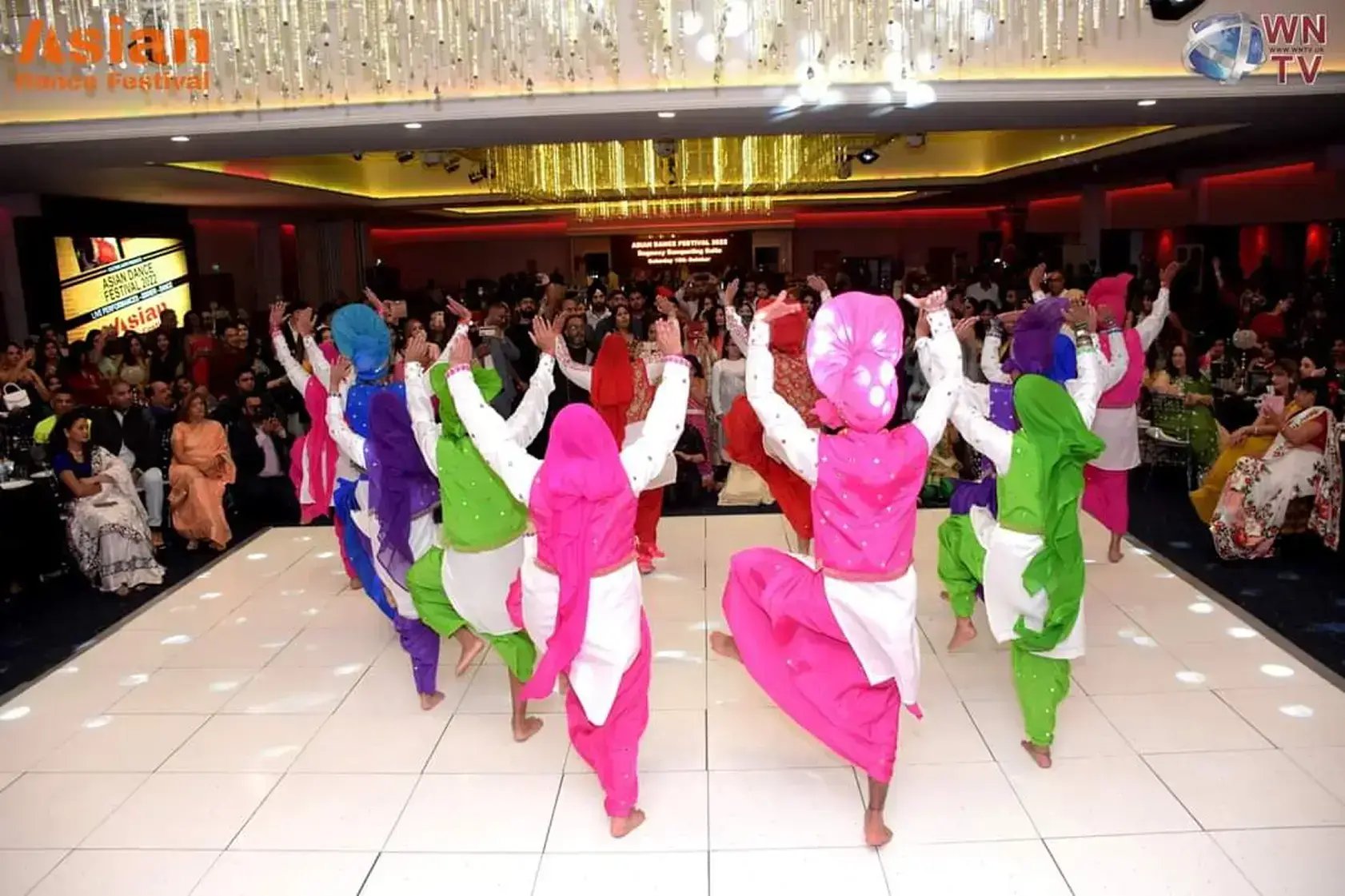Jodi Dancers performing a colourful Bhangra routine on a wedding reception dance floor in front of seated and standing guests.