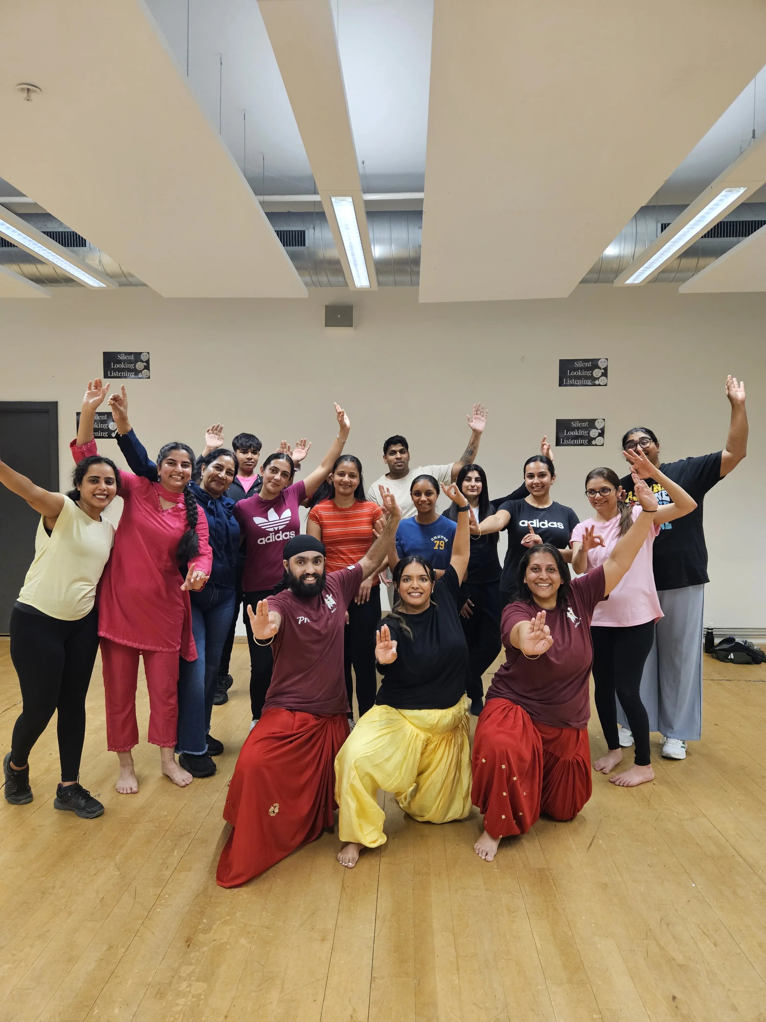 Group posing together after a Bhangra dance workshop in a studio, with three participants kneeling at the front in colourful Punjabi dancewear.